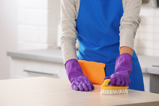 Woman cleaning table with brush in kitchen, closeup. Space for text