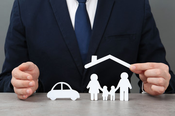 Man with cutout paper family, house roof and car at table, closeup. Life insurance concept