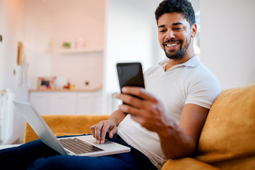 Handsome african american man using laptop and mobile phone at home.