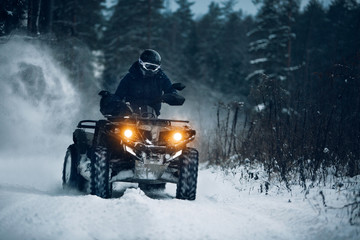 Rider driving in the quadbike in winter in the forest . Biker go fast at the winter forest with a...