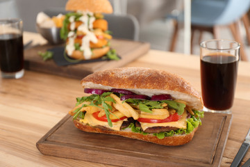 Wooden serving plate with yummy sandwich on table in cafe