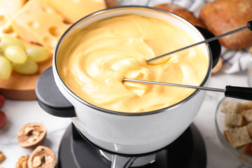Pot of delicious cheese fondue and forks on table