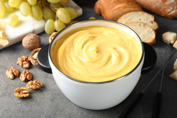 Pot with delicious cheese fondue on gray table