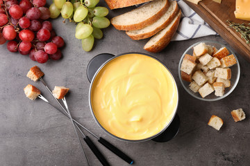 Flat lay composition with pot of delicious cheese fondue on gray table