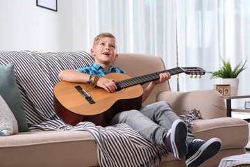 Cute little boy playing guitar on sofa in room