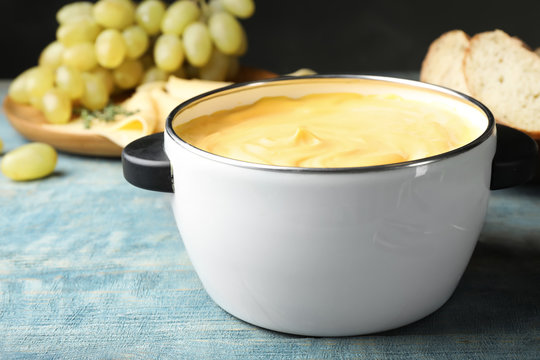 Pot with delicious cheese fondue on wooden table