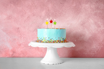 Fresh delicious birthday cake with candles on stand against color background