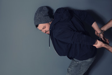 Man putting handcuffs on drug dealer against grey background. Space for text