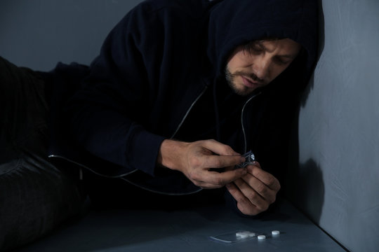 Young addicted man with drugs lying on floor
