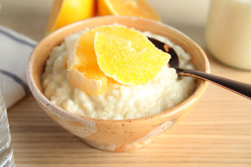 Creamy rice pudding with orange slices in bowl on wooden table