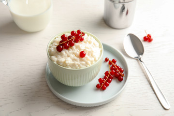 Creamy rice pudding with red currant in bowl served on white wooden table