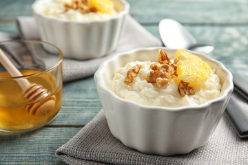 Creamy rice pudding with walnuts and orange slice in ramekin served on wooden table