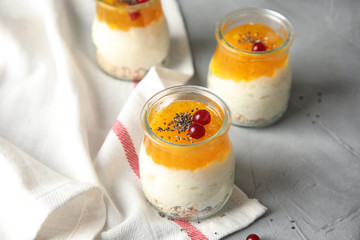 Creamy rice pudding with red currant, jam and oatmeal in jars on table