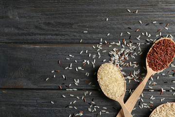 Flat lay composition with brown and other types of rice in spoons on wooden background. Space for text