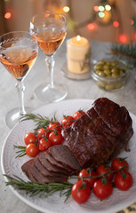 Cooked sliced roast beef with cherry tomatoes and glasses of wine in a festive decor
