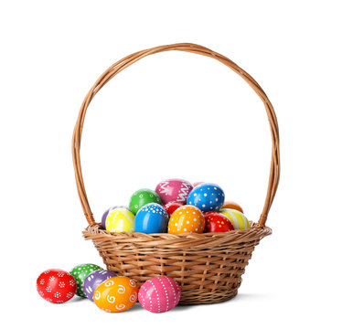 Decorated Easter eggs in wicker basket on white background