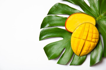 Fototapeta na wymiar Juicy mango and green tropical leaf isolated on white, top view. Space for text