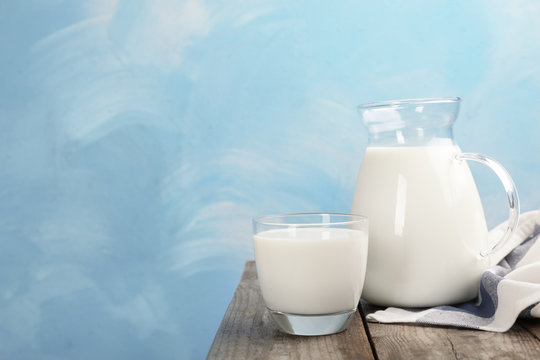 Glass and jug of fresh milk on wooden table against color background. Space for text