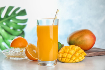 Glass of fresh mango drink and tropical fruits on table against color background