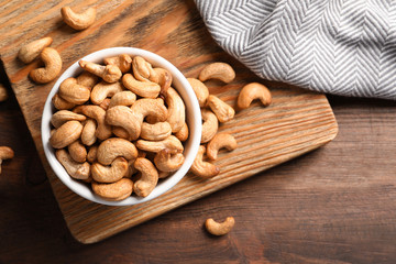 Tasty cashew nuts in bowl on wooden table, top view