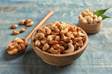 Tasty cashew nuts in bowl and spoon on wooden table