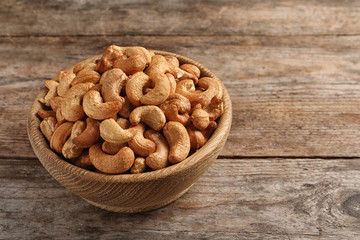 Tasty cashew nuts in bowl on wooden table. Space for text