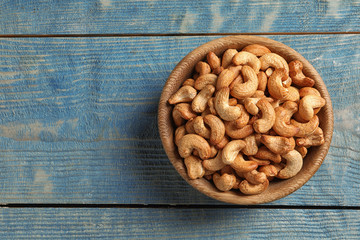 Tasty cashew nuts in bowl on color wooden table, top view. Space for text