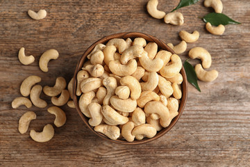 Tasty cashew nuts in bowl on wooden table, top view