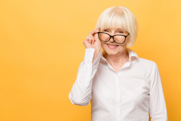 Joyful senior lady in glasses laughing isolated over yellow background. Friendly, mature white...