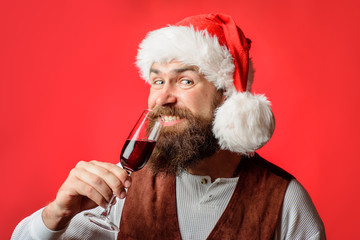 Happy bearded man in Santa hat toasting&celebrating New Year. Christmas New year party concept. Handsome Christmas Santa Claus holds wine glass in hands. Business man in Santa hat drinking red wine.