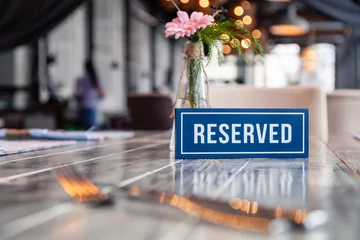 Foto op Aluminium Closeup wooden blue white rectangular plate with word Reserved standing on gray vintage table in restaurant near to setting, napkins, fork, knife, vase with flowers, glasses, ceramic white plates © Тимур Конев