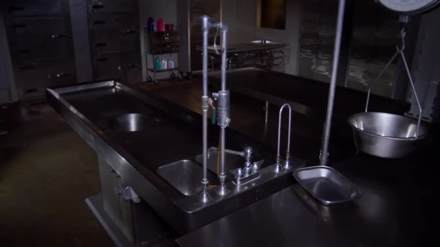 A COLD, EMPTY MORGUE WITH AN AUTOPSY TABLE IN THE FOREGROUND.  4K, 10 BIT SLIDER SHOT.