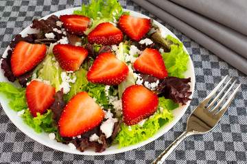 Vegetarian delicious fresh salad with purple and green lettuce leaves, strawberries and goat cheese on grey tablecloth.