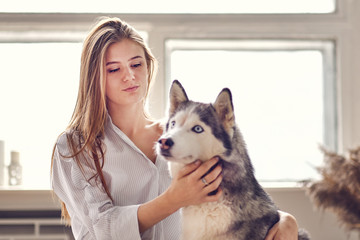 blonde girl playing with her dog husky at home.