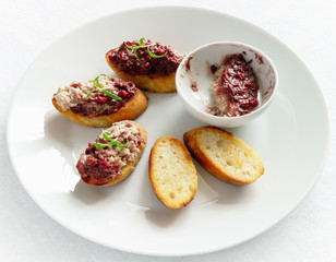 half emptied cup with rabbit rillettes toppled with cranberry red wine confiture and crostini with some slices spreaded with the rillette over 