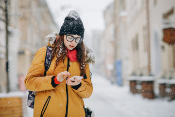 Portrait of beautiful happy young woman with smartphone over christmas lights in winter