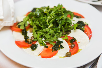 Tasty salad from tomatoes, cheese and arugula on white plate in the restaurant