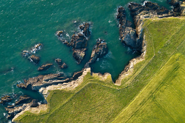 Rocky coast is washed by the ocean from above, green grass grows on the rocks. (2:3)