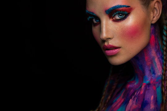 Fashion portrait of beautiful young woman with bright pink and blue colors, art make-up, face art on dark background