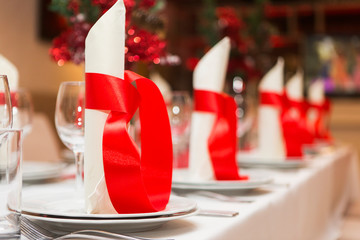 Beautiful decorations on the table in a restaurant. White plates with napkins and red tapes - obrazy, fototapety, plakaty