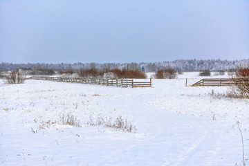 Snow-covered field in the countryside. A wooden fence of farmland.