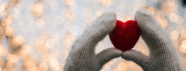 Female hands in knitted white mittens with heart of snow in winter day. Love and St. Valentine cozy...