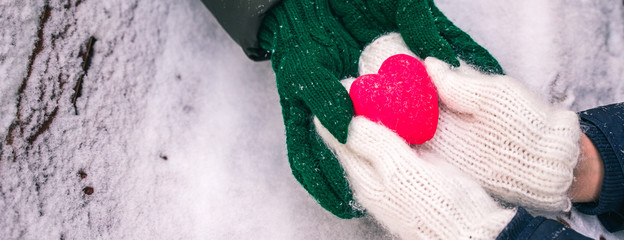 Hands in gloves holding heart closeup on winter snow background. Toned. Valentine's Day and love concept, banner