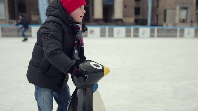 One little kid boy having fun with skates and plastic penguin. Happy children in winter clothes have fun skating on ice. Cold winter weather - Image