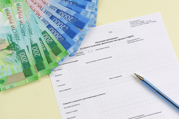 The blank form of the tax document in the Russian language "Declaration on the tax to incomes of physical persons (form 3-NDFL)", pen and new ruble banknotes