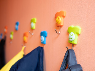 funny smiling colored hangers for children kids apparel on orange wall. at kindergarten, nursery...