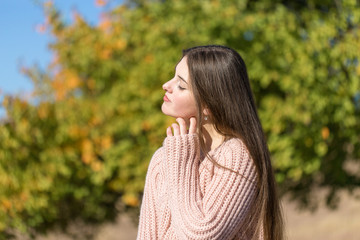 Portrait of pretty young woman in stylish knitted sweater standing on the golden autumn forest on sunny day	