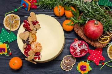 Homemade Christmas cheesecake on black wooden bacground decorated by orange, cookies, pomegranate, rosemary. Moist and smooth classic baked New York cheesecake.