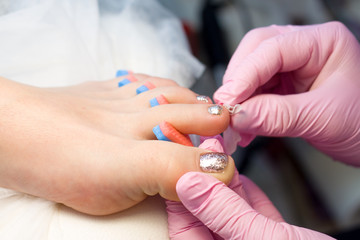 Nail Care And pedicure concept. Closeup Manicurist hands in pink gloves is Painting gold Nail Polish On Client's toes. Woman In Beauty Salon.
