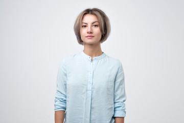 Young woman with short hairstyle wearing blue t-shirt standing with neutral expression. Photo for...